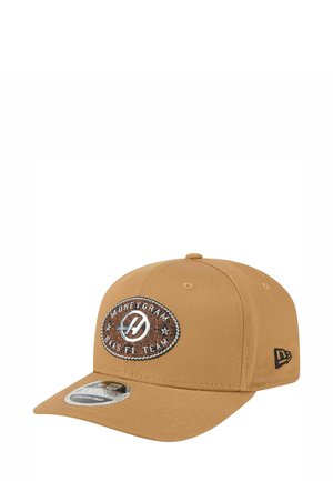 Tan baseball cap with a curved brim, featuring a brown and silver oval patch reading "MoneyGram Haas F1 Team" and a black logo on the side.