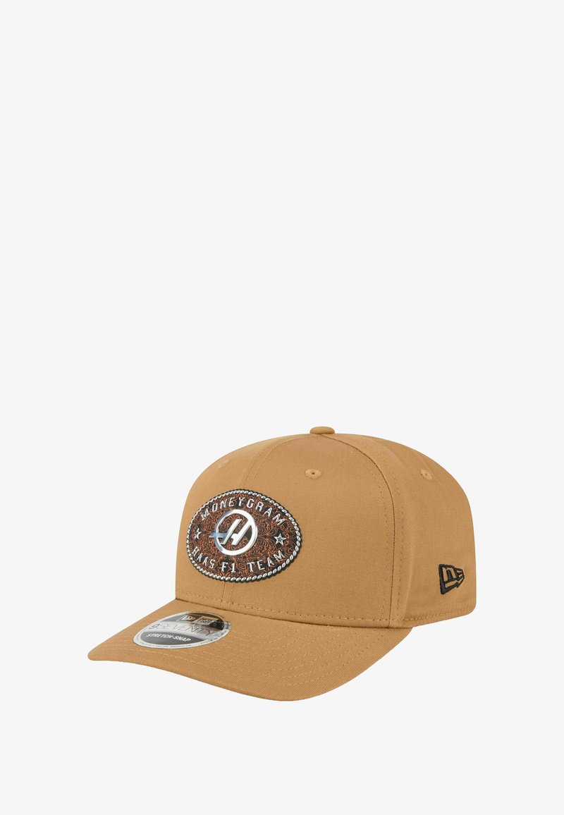 Beżowa czapka baseballowa z wygiętym daszkiem, z brązową i srebrną owalną naszywką z napisem "MoneyGram Haas F1 Team" oraz czarnym logo z boku.