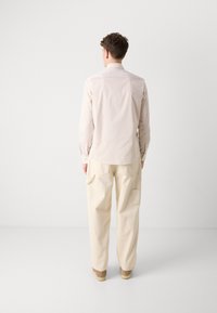 Camicia a righe rosa chiaro con colletto classico, abbinata a pantaloni cargo beige a vestibilità ampia. L'outfit presenta tasche laterali.
