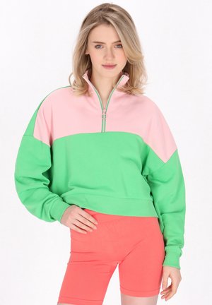 Grøn og pink lynlåstrøje med farveblokdesign; blødt stof, løs pasform, ribstrikkede manchetter og en halv lynlås ved nakken.