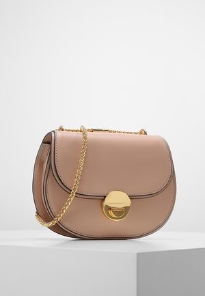 Bolso bandolera de cuero beige con solapa curva, cierre circular dorado y correa de cadena dorada a juego sobre superficie blanca.