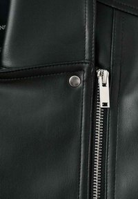 Część czarnej skórzanej kurtki z widocznym srebrnym suwakiem i zatrzaskiem. Gładka faktura z widocznym przeszyciem wzdłuż krawędzi.