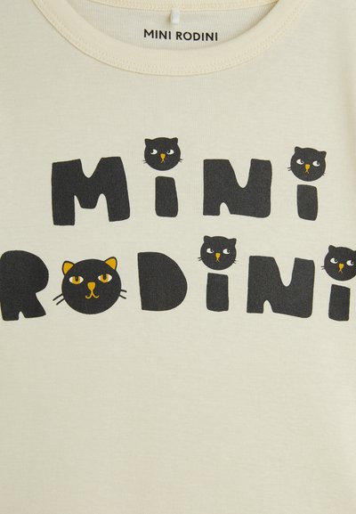 Die cremefarbene T-Shirt mit kurzen Ärmeln zeigt auffällige schwarze Buchstaben "MINI RODINI" und verspielte Katzengrafiken. Es besteht aus weicher Baumwolle mit einer glatten Textur.