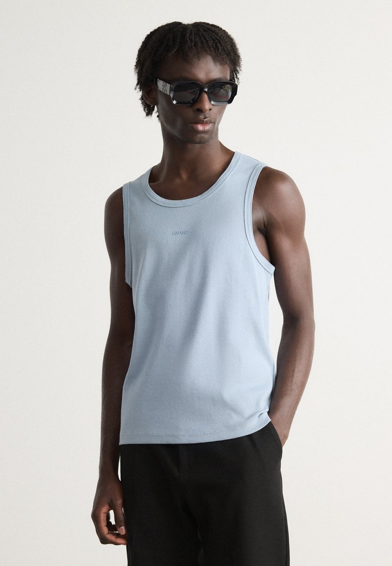 Débardeur à rayures bleu clair avec un col rond, affichant un petit logo au centre et des lunettes de soleil noires qui complètent le design.