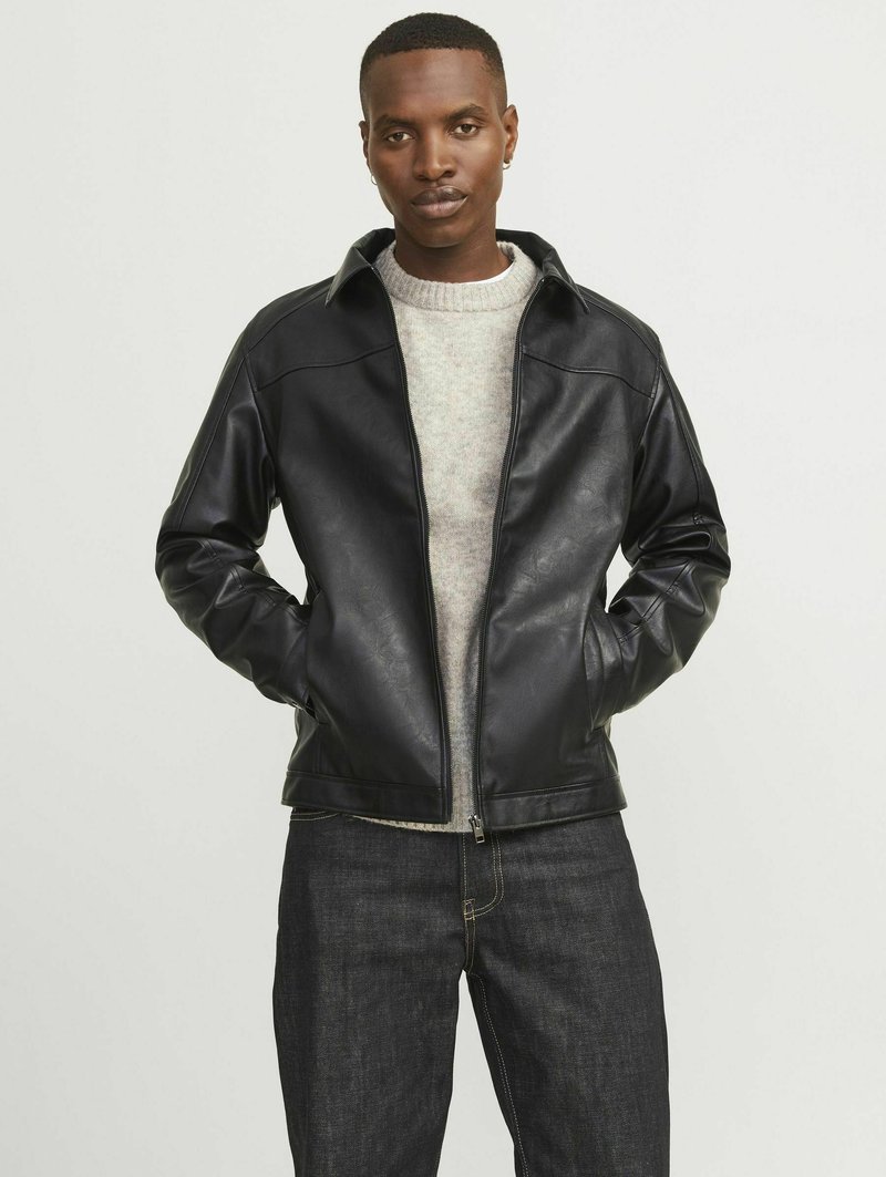 Chaqueta de cuero negra con cierre de cremallera y cuello, que presenta una textura suave, situada sobre un fondo neutro. Lleva puesta una sudadera gris.