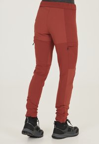 Röda, elastiska vandringsbyxor med dragkedjefickor, förstärkta knän och en avsmalnande passform, i kombination med svarta vandringsskor som når ankeln.