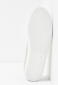 Semelle de sneaker blanche en caoutchouc texturé, avec une tige métallique tissée et une taille marquée comme 37. Vue de côté inclinée.