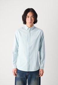 Light blue striped button-up shirt with long sleeves and a collar, featuring a small logo on the chest and a smooth cotton texture.