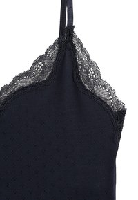 Débardeur marine avec des bretelles réglables, une dentelle au niveau du col, et un tissu texturé avec de petits points en relief.