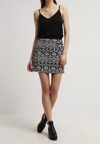 Top senza maniche nero abbinato a una gonna mini aderente con un motivo geometrico bianco. Indossato con scarpe nere con lacci.