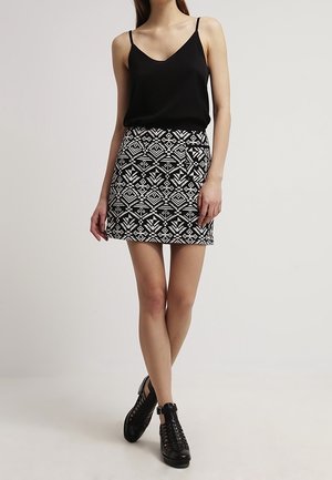 Haut sans manches noir associé à une mini-jupe ajustée présentant un motif géométrique blanc. Porté avec des chaussures noires à lacets.