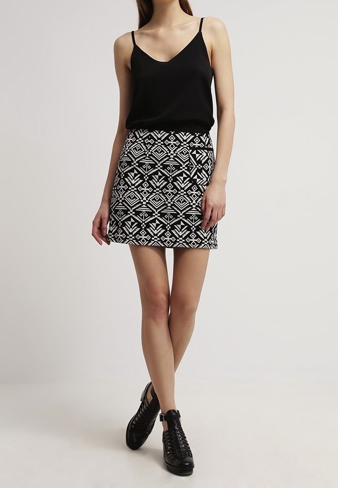 Top senza maniche nero abbinato a una gonna mini aderente con un motivo geometrico bianco. Indossato con scarpe nere con lacci.