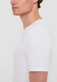 T-shirt bianco a maniche corte realizzato in morbido cotone, con scollatura a girocollo e design aderente, esposto su uno sfondo neutro.