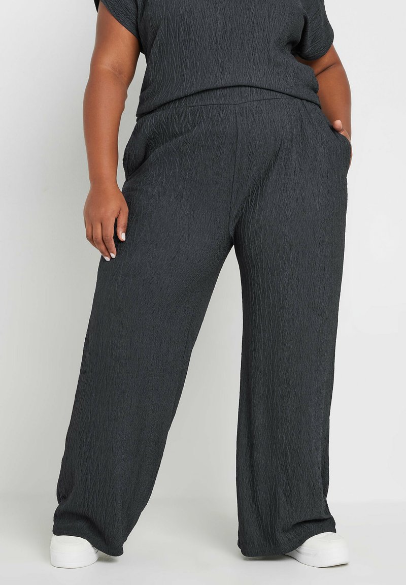 Czarne, teksturowane spodnie typu wide-leg z diagonalnymi wzorami, elastycznym pasem i bocznymi kieszeniami. Połączone z dopasowaną górą i białymi sneakersami.