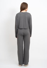 Completo grigio con maglietta a maniche lunghe e pantaloni realizzato in un tessuto morbido. La maglietta ha un taglio corto, mentre i pantaloni sono ampi con una superficie liscia.