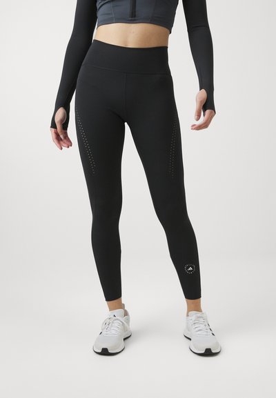 Leggings deportivos negros hechos de una tela elástica, con perforaciones laterales, una cintura alta y un detalle de logo en la parte inferior de la pierna.