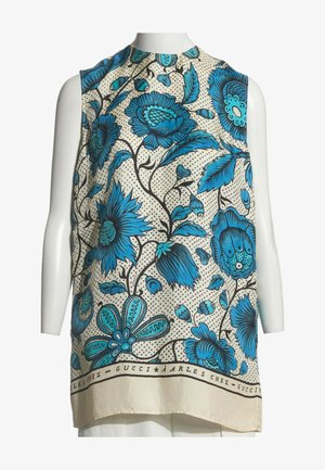 Mouwloze beige top met grote blauwe bloemmotieven en zwarte takken, tentoongesteld op een witte mannequintorso.