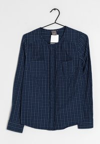 Navyblaue button-up Hemd mit weißem Karomuster, zwei Brusttaschen, langen Ärmeln und rundem Halsausschnitt. Leichtes Gewebe hängt an einem schwarzen Haken.