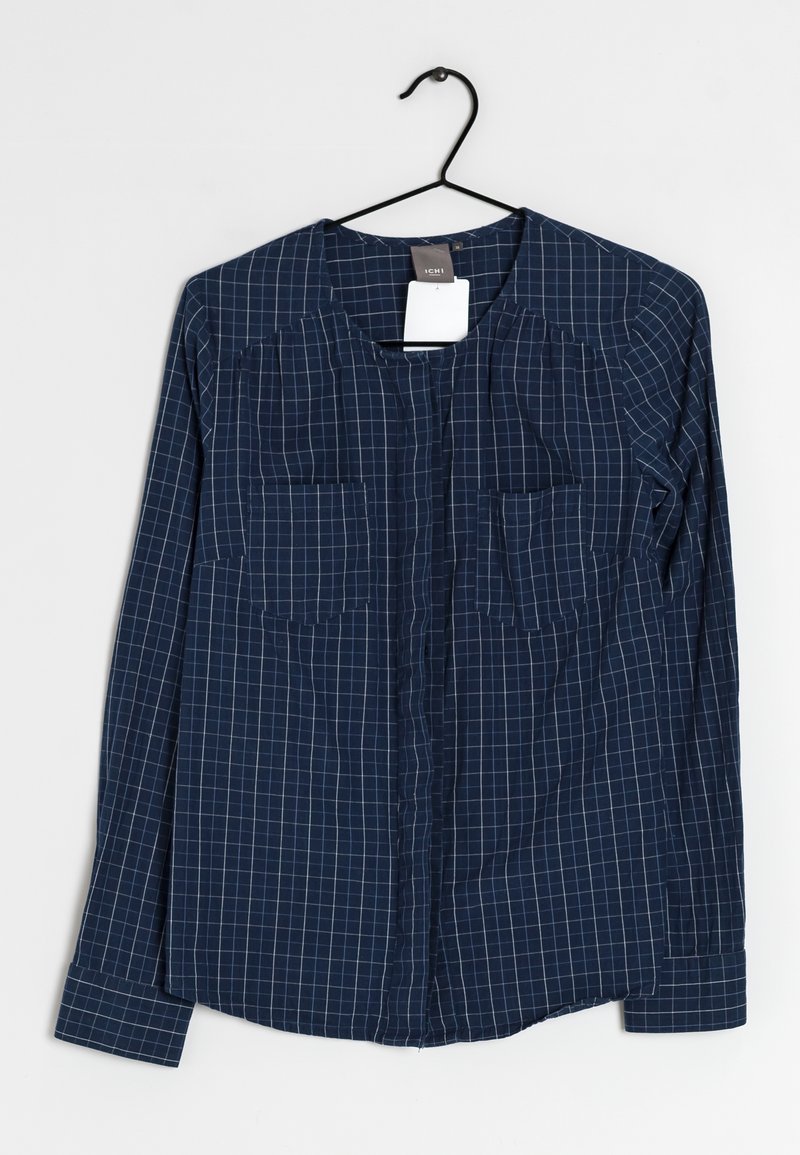 Navyblaue button-up Hemd mit weißem Karomuster, zwei Brusttaschen, langen Ärmeln und rundem Halsausschnitt. Leichtes Gewebe hängt an einem schwarzen Haken.