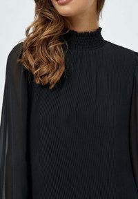 Svart blus med en smockad hög hals, plisserad textur och genomskinliga långa ärmar för ökad elegans och visuell kontrast.