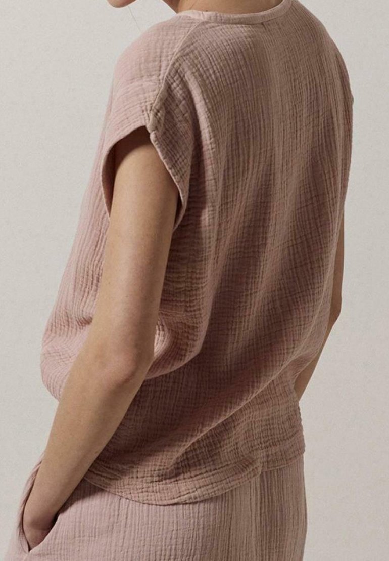 Top rosa, testurizzato, realizzato in tessuto leggero. Vestibilità morbida con maniche corte e orlo curvo. Presenta una leggera rigatura e un design rilassato.