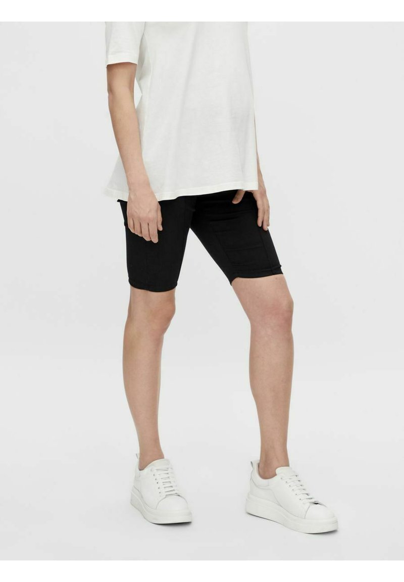 Shorts in denim nero con una vestibilità slim, caratterizzati da una superficie liscia e dettagli di cucitura sottili, abbinati a una t-shirt bianca ampia e a sneakers bianche.