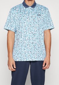 Polo à imprimé floral en bleu clair avec un col bleu foncé. Manchettes courtes et logo de la marque discret sur la poitrine. Tissu texturé.
