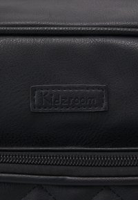 Černá kožená taška s texturovaným povrchem, zipovým uzávěrem a našitým štítkem s embosovaným nápisem "Kidzroom".