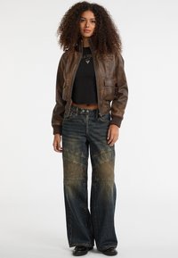 Bruine leren bomberjack, zwarte cropped top, wijde blauwe denim jeans met textuurpanelen, en zwarte schoenen.