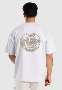 Camiseta de manga corta en gris claro que presenta un gran gráfico de un globo marrón y texto en la parte posterior. Hecha de un suave material de algodón texturizado.
