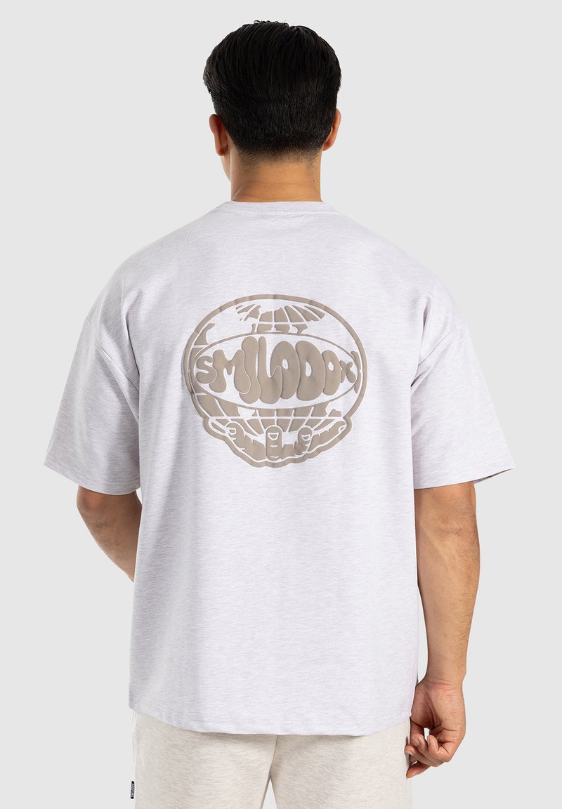 Ljust grå kortärmad t-shirt med en stor brun globgrafik och text på baksidan. Tillverkad av mjukt, texturerat bomullsmaterial.