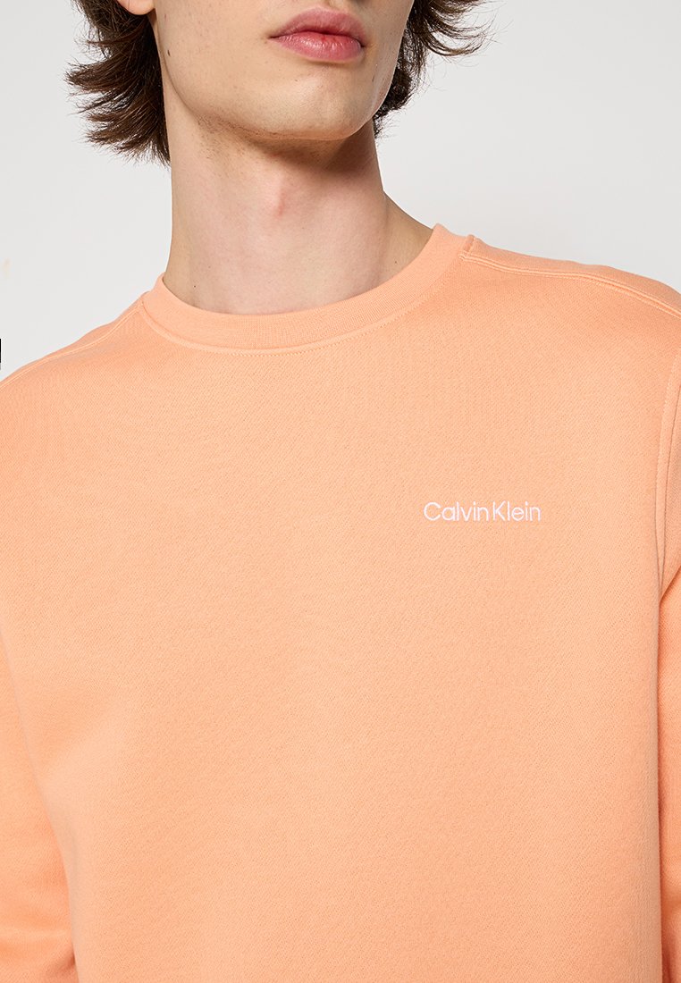 Sweatshirt cropped orange clair en matériau doux. Doté d'un col rond et d'un petit logo blanc "Calvin Klein" sur la poitrine.