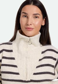 Maglione in felpa con colletto alto, mezza zip, colore crema con strisce orizzontali marroni scure, texture morbida e dettagli a coste.