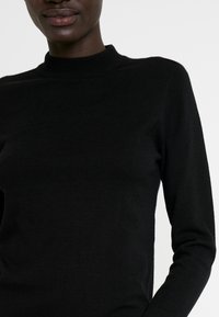 Pull noir à manches longues avec col montant, fabriqué en matière douce et finement tricotée ; présente une texture lisse et une coupe ajustée.