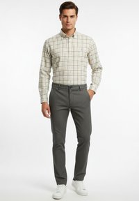 Camisa de botones en beige con patrón de cuadrícula, combinada con pantalones texturizados gris oscuro y zapatillas blancas. Diseño sencillo y entallado.