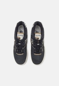 Paire de baskets New Balance 550 noires avec des accents blancs et beiges, vues de dessus sur un fond blanc uni.