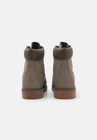Botas de cuero gris con un collar suave y acolchado, punta redondeada y suela de goma marrón. La vista trasera destaca la costura y los materiales texturizados.