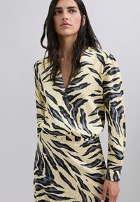 Blusa amarilla con rayas de tigre negras, con escote en V y cierre frontal de botones. Mangas largas y tejido ligero y suave.