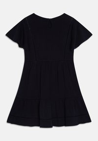 Černé šaty s krátkými volánovými rukávy, texturovaná tkanina, rozšířený silueta a vícestupňový lem. Uzávěr na zádech s klíčovou dírkou a detailem knoflíku.