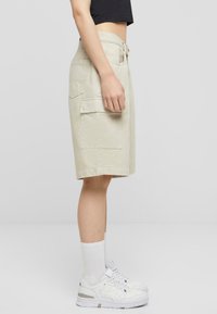 Beige cargo shorts med sidelommer, belteholdere og rett snitt. Kombinert med hvite joggesko og ankelsokker.