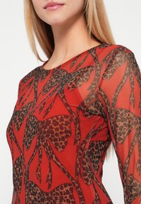 Przezroczysta bluzka z długim rękawem w intensywnym czerwonym kolorze, zdobiona odważnym wzorem w leoparda w czerni i brązie. Gładka faktura oraz dopasowany krój.