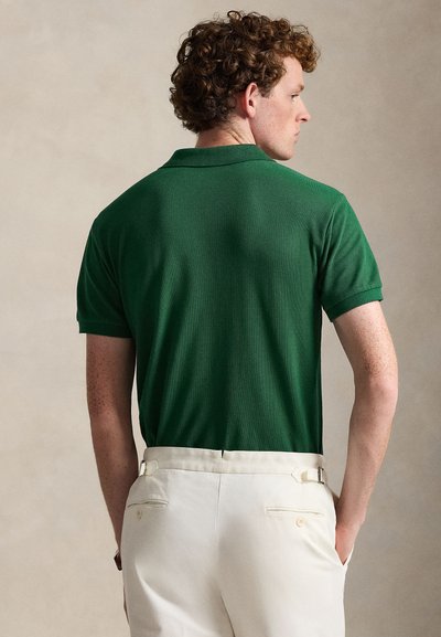 Πράσινο πόλο μπλουζάκι με υφή υφάσματος, κοντά μανίκια και κλασικό γιακά, σε συνδυασμό με κρεμ παντελόνι που διαθέτει πίσω τσέπες και θηλιές για ζώνη.