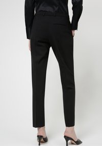 Czarne dopasowane spodnie o gładkiej fakturze, bez zdobień, z jedną tylną kieszenią. W zestawieniu z czarnymi szpilkami.