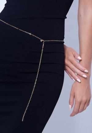 Ceinture en chaîne dorée présentant des maillons allongés, drapée sur une robe noire cintrée, avec un accent décoratif allongeant sa longueur.