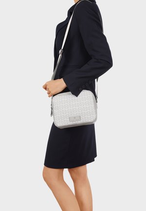 Donna con blazer nero e gonna che porta una borsa tracolla bianca con motivo e tracolla regolabile sulla spalla.