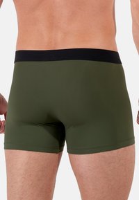 Boxer verde con vita nera, caratterizzati da una superficie liscia e un design aderente, mostrano la vista posteriore e dettagli di cucitura minimi.
