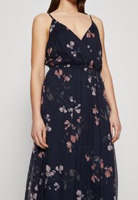 Marinblå blommig maxiklänning med justerbara spaghetti band, prydd med rosa och vita blommönster, elastisk midja och en flödande kjol.