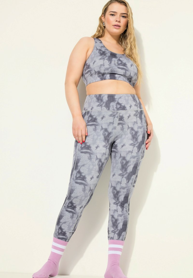 Conjunto de sujetador deportivo y leggings en un suave tejido de tie-dye gris, con un diseño ceñido y una cinturilla ancha; combinado con calcetines de rayas rosas.