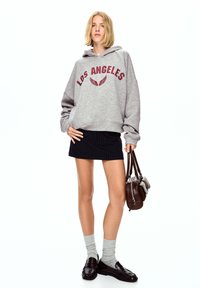 Šedá mikina s nápisem "LOS ANGELES" v burgundské barvě, zkombinovaná s černou sukní s pruhy. Doplněno šedými ponožkami a tmavými loaferkami. Přítomná hnědá kabelka.