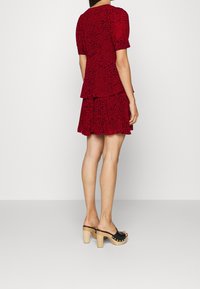 Rotes, kurzärmeliges Kleid mit schwarzem Leopardenmuster, am Saum geschichtet. Kombiniert mit schwarzen Clogs mit offenem Zehenbereich und Holzabsatz.